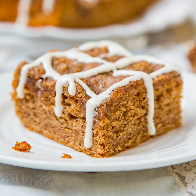A slice of carrot cake with white icing drizzle on a white plate.