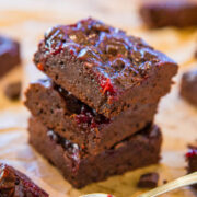 Stack of chocolate brownies with raspberry topping, accompanied by a spoonful of raspberry sauce.