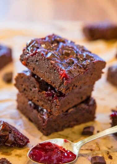 Stack of chocolate brownies with raspberry topping, accompanied by a spoonful of raspberry sauce.