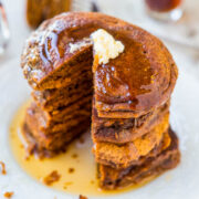 A stack of pumpkin pancakes with a pat of butter and syrup on top, with a cup of coffee in the background.