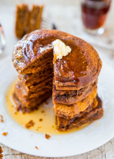 A stack of pumpkin pancakes with a pat of butter and syrup on top, with a cup of coffee in the background.