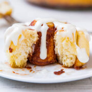 A cinnamon roll with icing on a white plate.