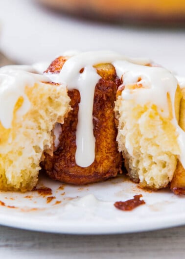 A cinnamon roll with icing on a white plate.