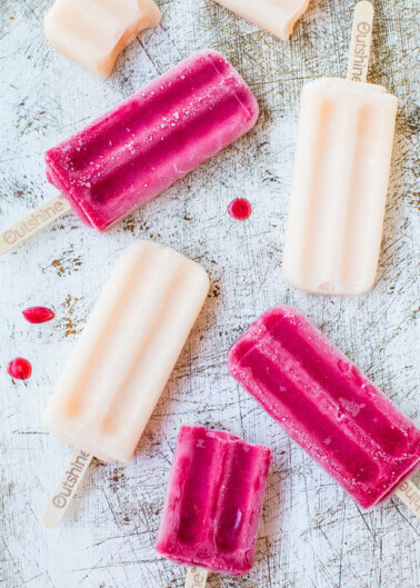 Six assorted popsicles on a textured surface with visible droplets.