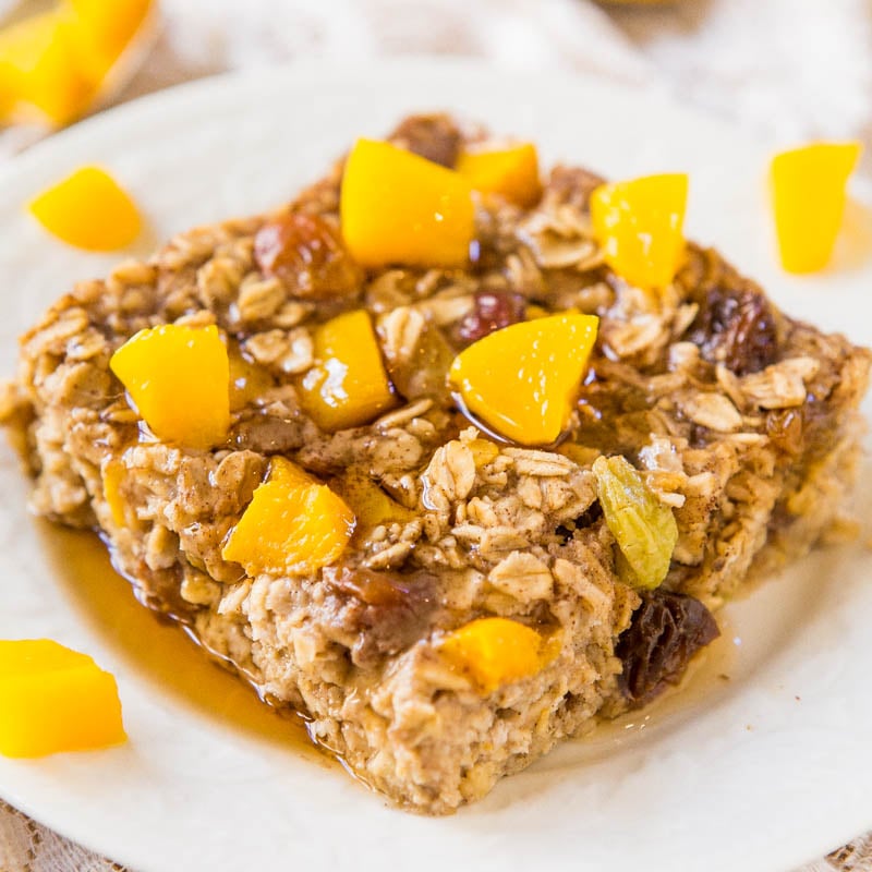 A baked oatmeal square topped with diced peaches and drizzled with honey on a white plate.