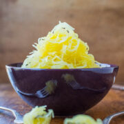 Cooked spaghetti squash served in a dark bowl with forks around it.