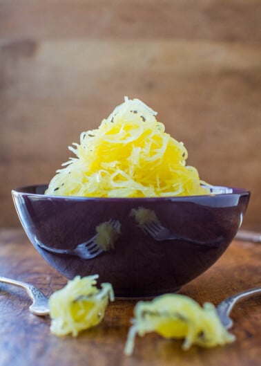 Cooked spaghetti squash served in a dark bowl with forks around it.