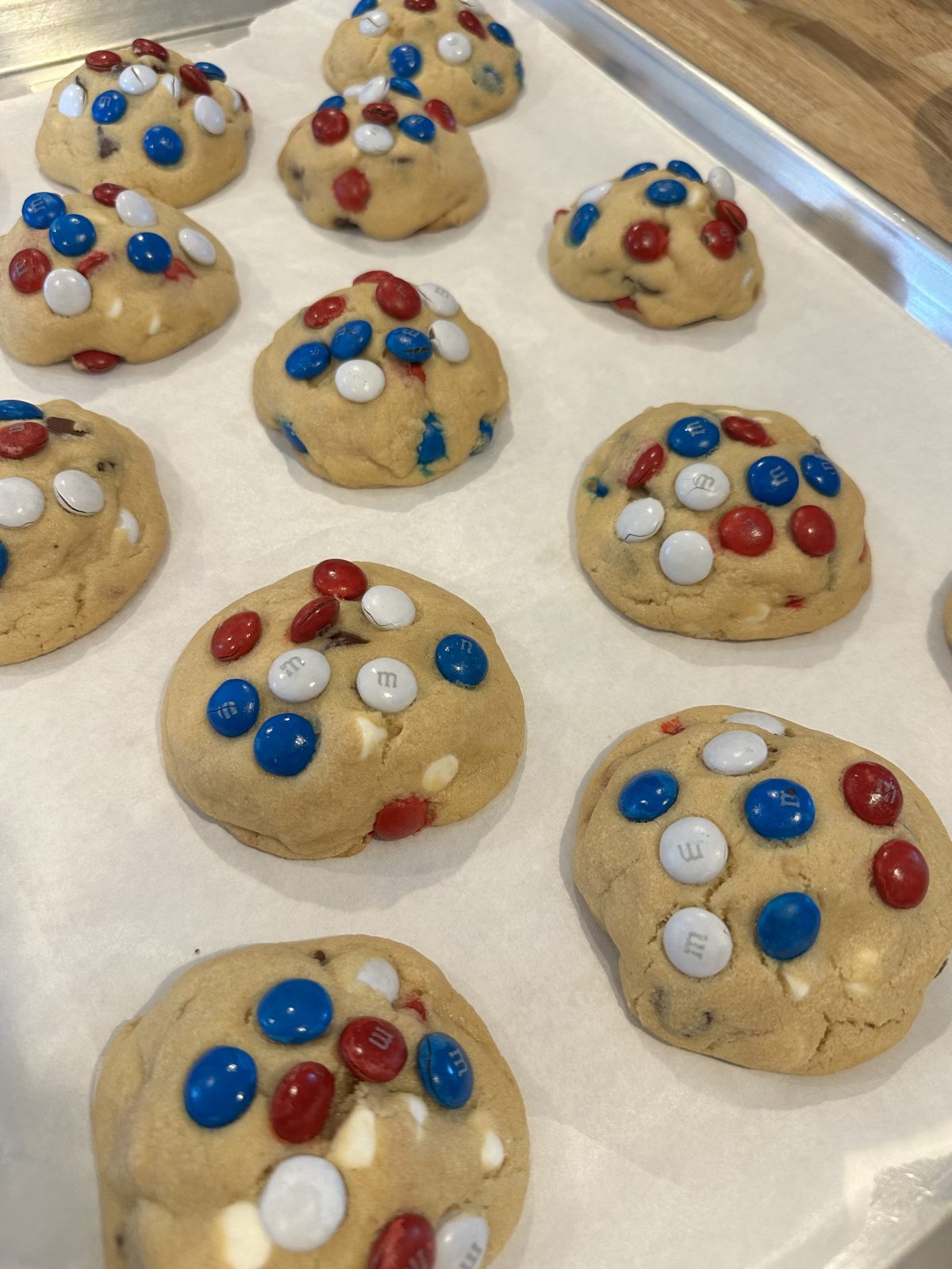 A tray of unbaked cookies with red, white, and blue candy-coated chocolates on parchment paper, ready to be baked.