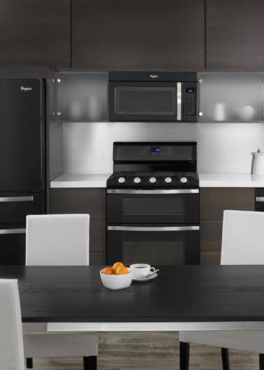 Modern kitchen with black appliances, dark cabinetry, and a dining table set for four.