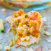 A corn chip topped with cheese, tomato, and corn salsa on a distressed metal surface.