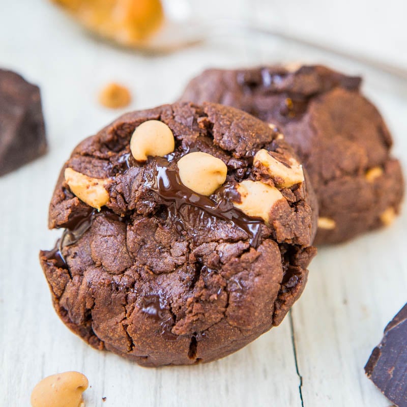 A chocolate cookie with melting chocolate chips and peanut butter chips on a wooden surface.