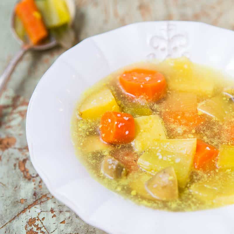 A bowl of vegetable soup with carrots and potatoes on a rustic table.