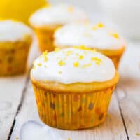 Lemon cupcakes with white icing and yellow sprinkles on a wooden surface.