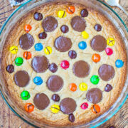 A freshly baked cookie cake studded with colorful candies and chocolate pieces in a glass dish.