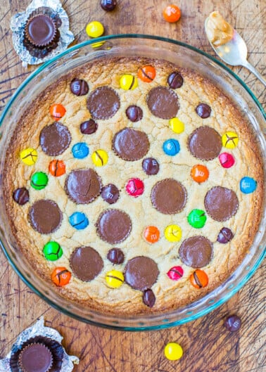 A freshly baked cookie cake studded with colorful candies and chocolate pieces in a glass dish.