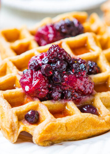 A freshly baked waffle topped with berry compote, served on a white plate.