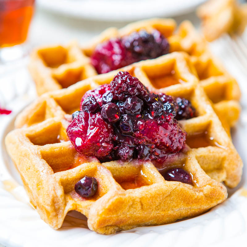 A freshly baked waffle topped with berry compote, served on a white plate.