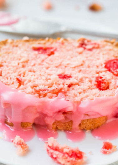 A slice of pink frosted cake with visible chunks of fruit on a white plate.