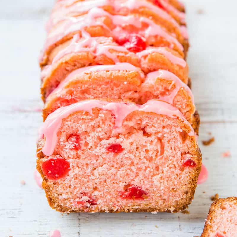 A sliced strawberry loaf cake with pink icing on a white surface.