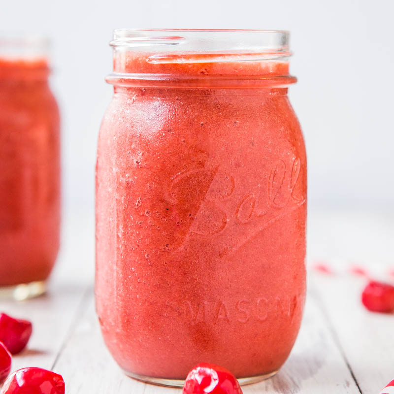 A mason jar filled with a pink smoothie on a light background.