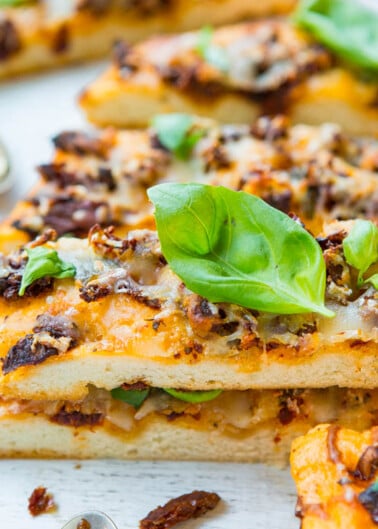 Slices of pizza with melted cheese, basil leaves, and a topping that resembles ground meat on a white surface.