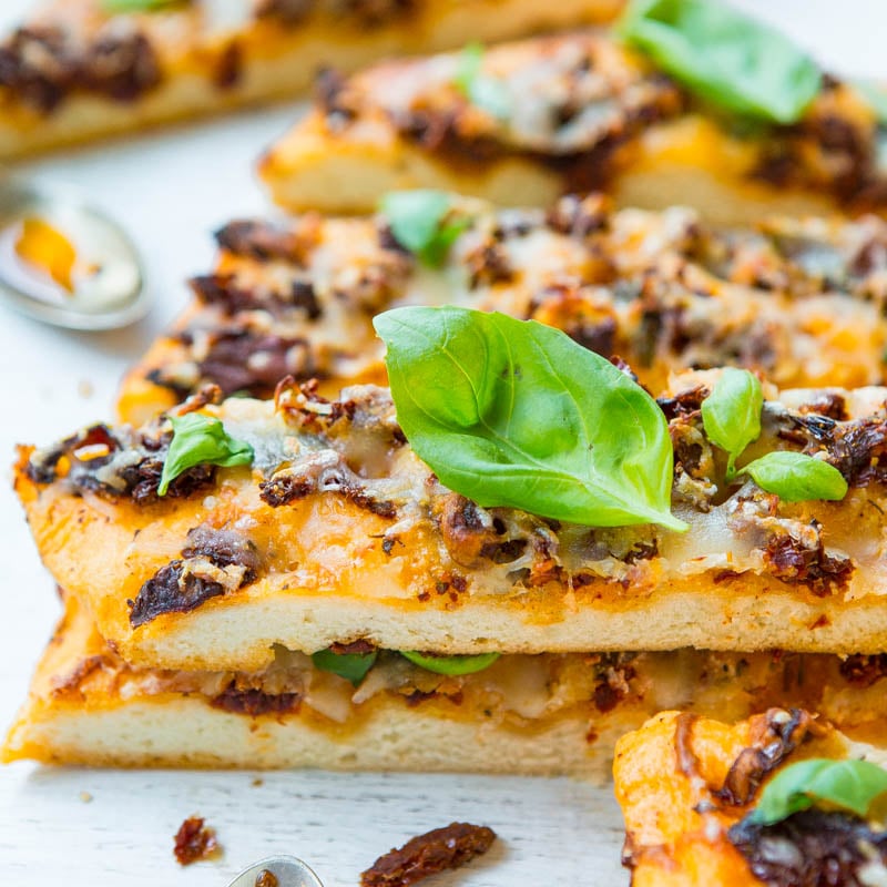 Slices of pizza with melted cheese, basil leaves, and a topping that resembles ground meat on a white surface.