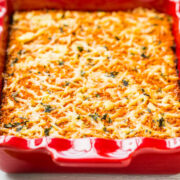 Baked lasagna in a red ceramic dish garnished with basil leaves.