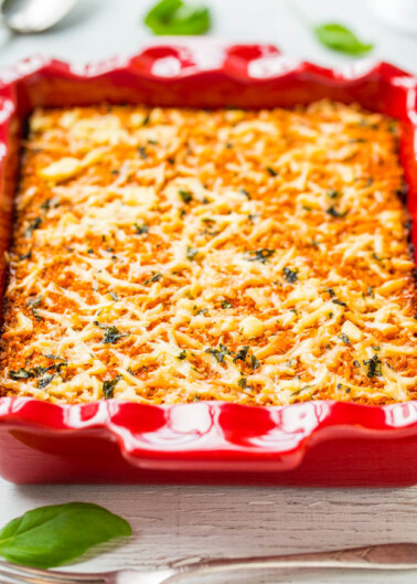 Baked lasagna in a red ceramic dish garnished with basil leaves.