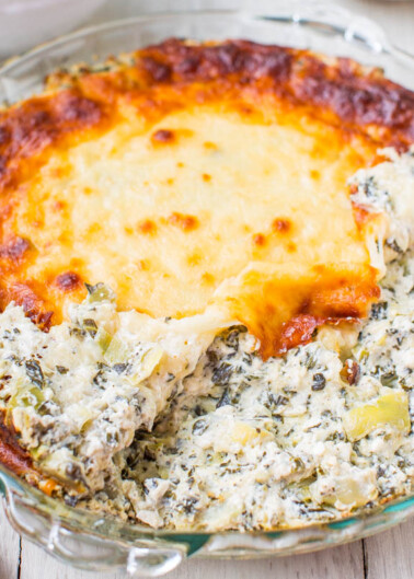 A baked spinach and cheese casserole in a glass dish with a portion scooped out.