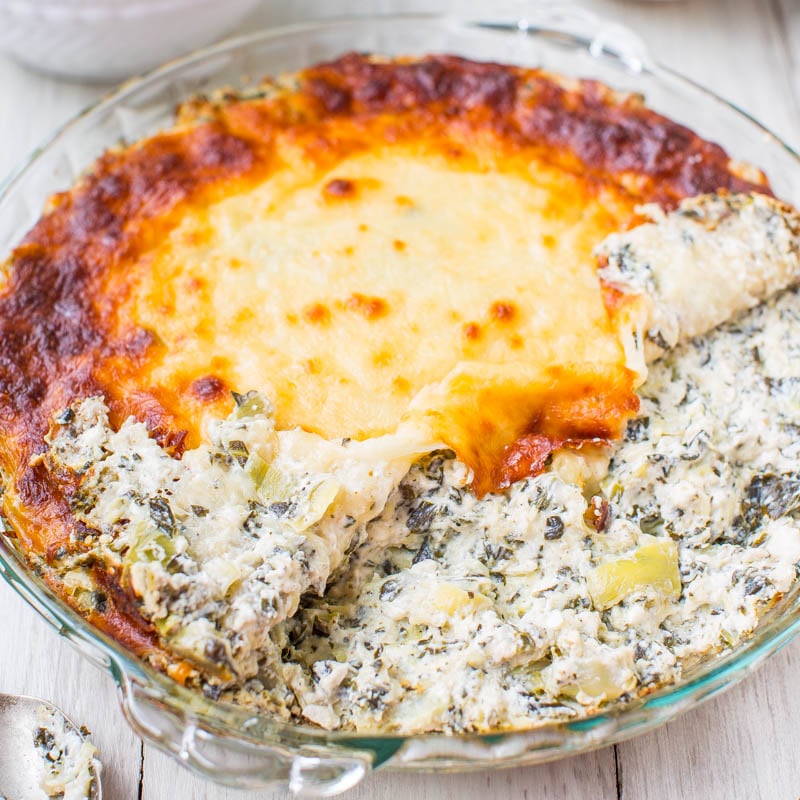 A baked spinach and cheese casserole in a glass dish with a portion scooped out.