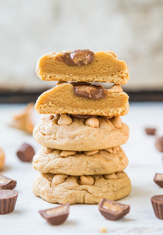 stack of four peanut butter cookies with peanut butter cups. the top cookie has been cut in half. 