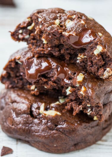 A stack of chocolate cookies with melting chocolate chunks and nuts.