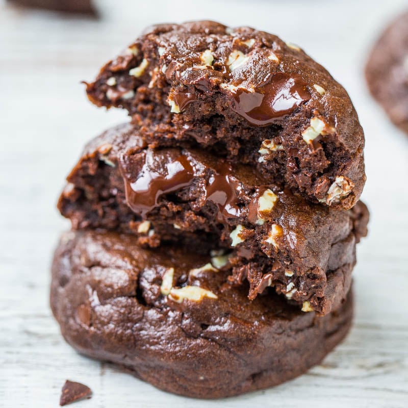 A stack of chocolate cookies with melting chocolate chunks and nuts.