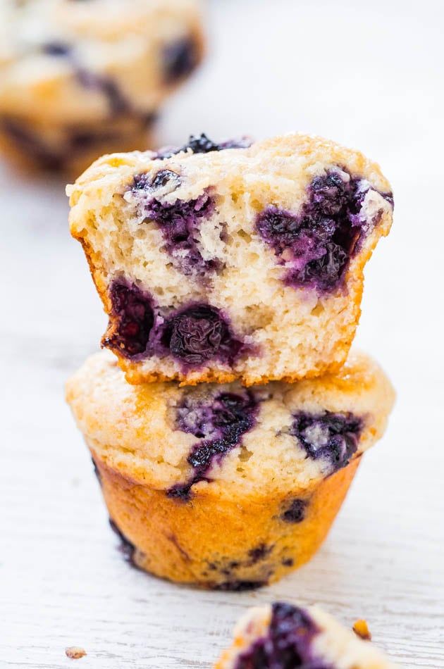 two blueberry muffins stacked on top of each other, the top one missing a bite