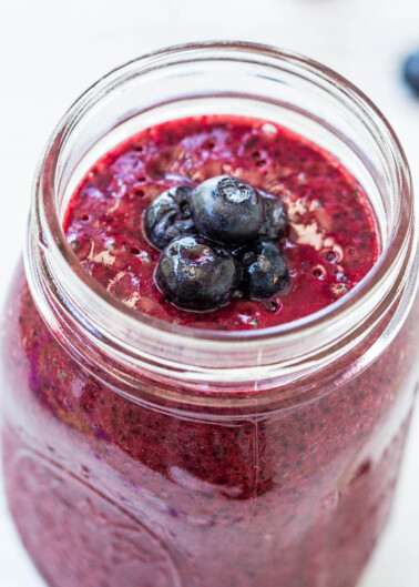 A fresh blueberry smoothie in a glass jar topped with whole blueberries.