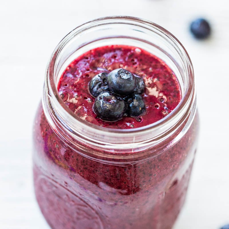 A fresh blueberry smoothie in a glass jar topped with whole blueberries.