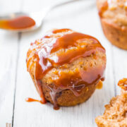 Freshly baked muffin drizzled with caramel sauce on a white wooden surface.