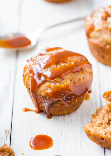 Freshly baked muffin drizzled with caramel sauce on a white wooden surface.