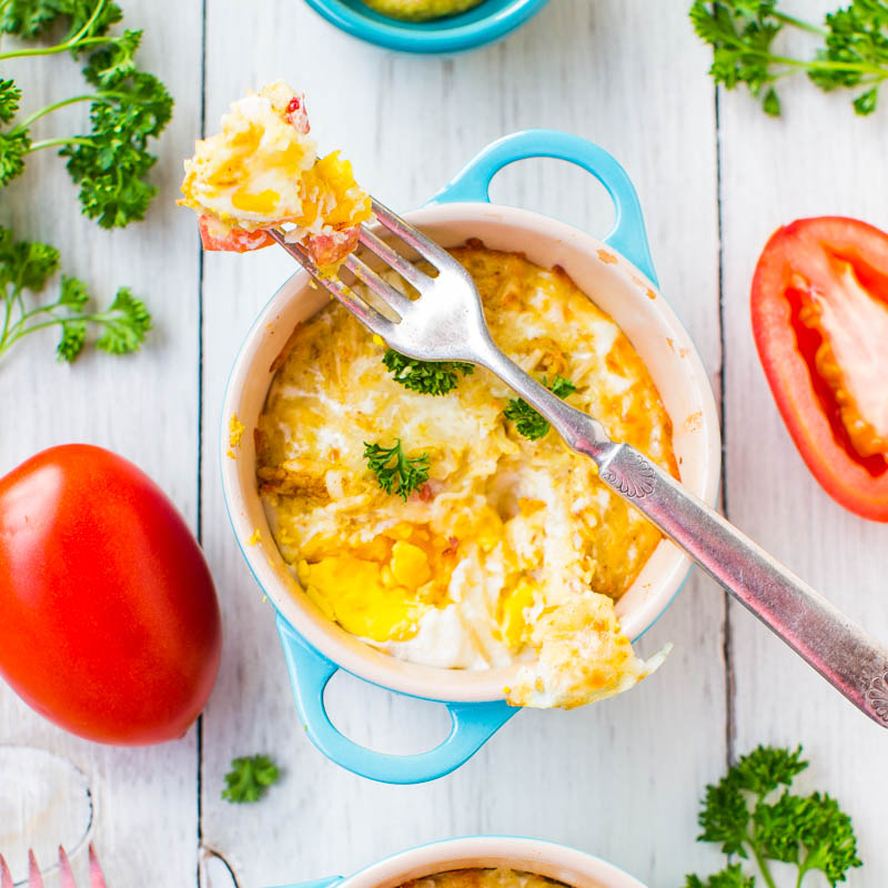 Baked egg dish in a blue ramekin with a fork and fresh vegetables on a wooden surface.