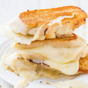 Stack of grilled cheese sandwiches with melted cheese on a white plate.