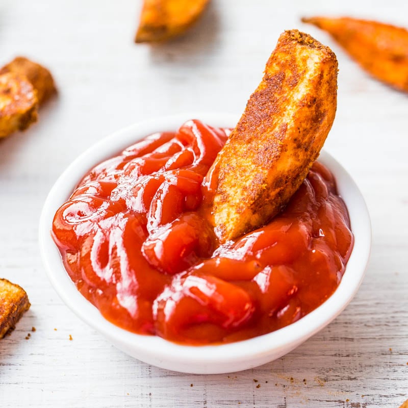 A seasoned potato wedge dipped in a bowl of ketchup.