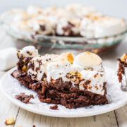 A slice of s'mores brownie pie with marshmallows on top, served on a white plate.