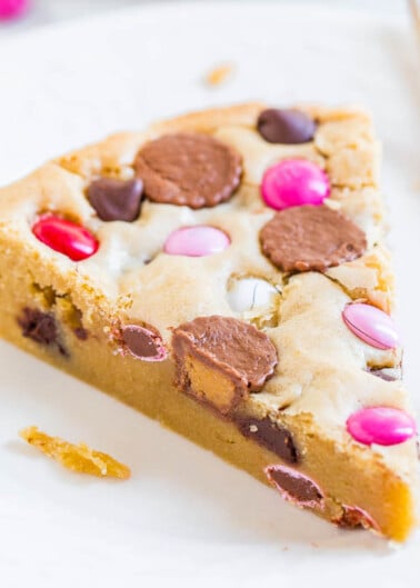 A slice of cookie cake with colorful candy pieces on a white plate.