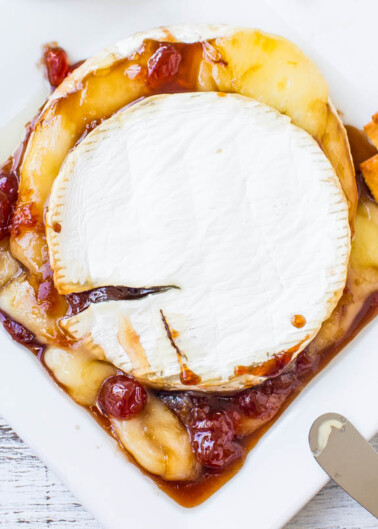 A wheel of brie cheese topped with jam and accompanied by crackers on a plate.