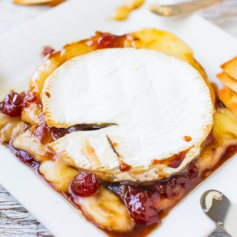 Baked brie cheese with cranberry sauce on a white plate.