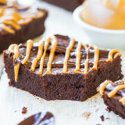 A chocolate brownie with caramel drizzle on a white wooden surface.