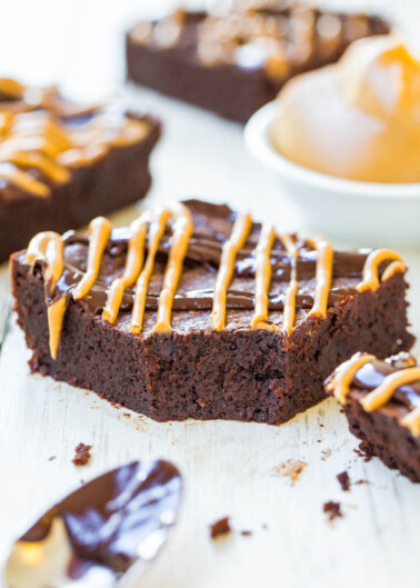 A chocolate brownie with caramel drizzle on a white wooden surface.