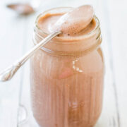 A glass jar filled with creamy chocolate spread, with a spoon resting on top showcasing the texture.