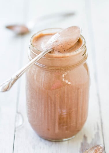 A glass jar filled with creamy chocolate spread, with a spoon resting on top showcasing the texture.