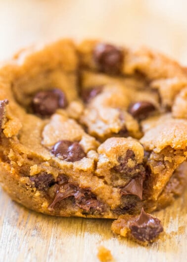 A close-up of a chocolate chip cookie with melted chocolate chips on a wooden surface.